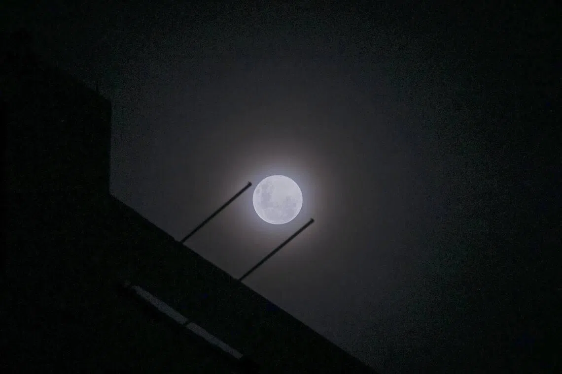 Wolf supermoon peers through cloudy night sky above Singapore